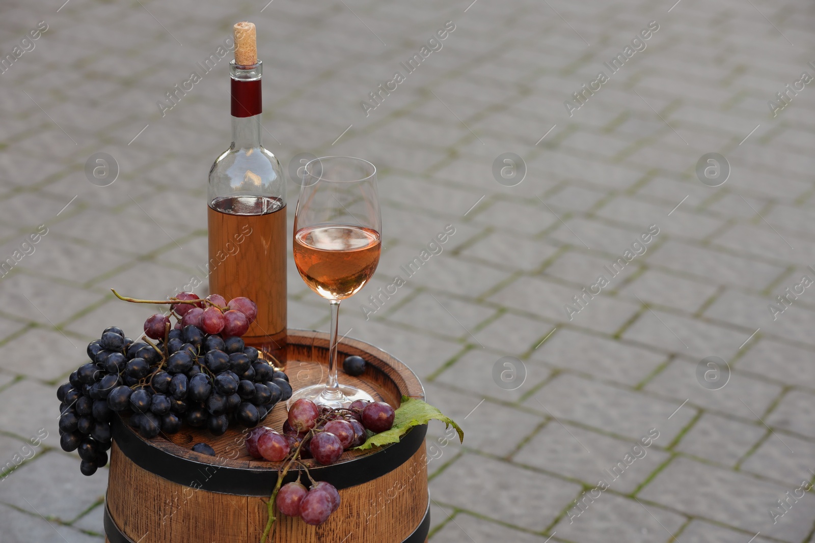 Photo of Delicious wine and ripe grapes on wooden barrel outdoors, space for text