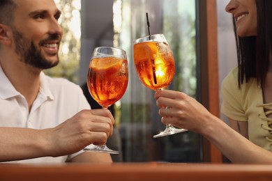 Photo of Couple clinking glasses of Aperol spritz cocktails outdoors, closeup