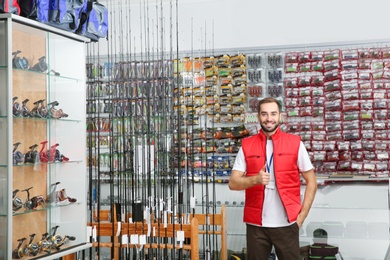 Photo of Salesman standing near showcase with fishing equipment in sports shop. Space for text