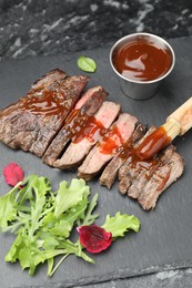Photo of Pieces of delicious roasted beef meat with sauce and greens on black table, closeup