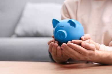 Couple with piggy bank at wooden table, closeup. Space for text