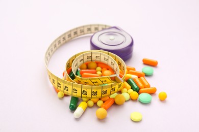 Photo of Many different weight loss pills and measuring tape on violet background
