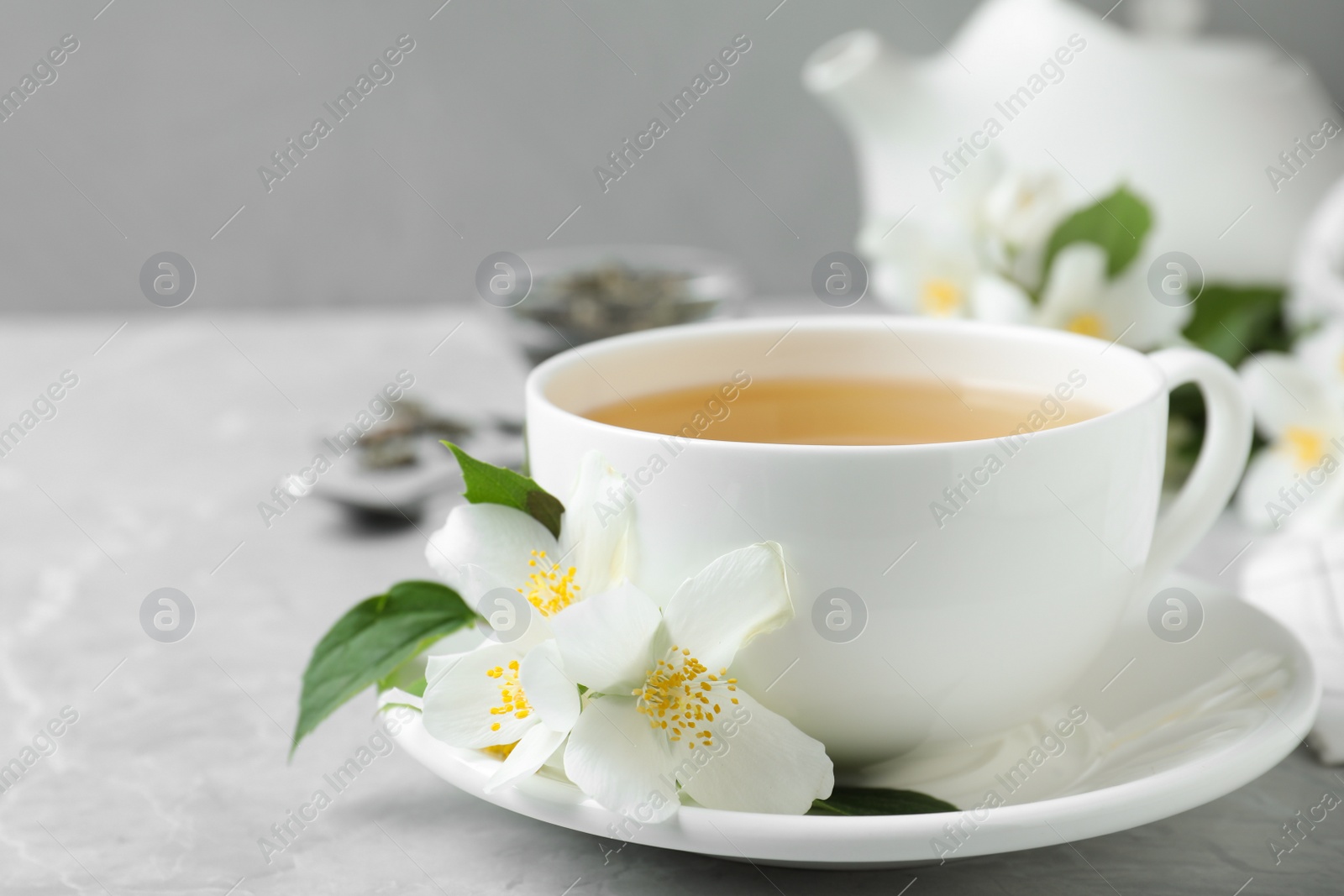 Photo of Cup of tea and fresh jasmine flowers on light grey marble table