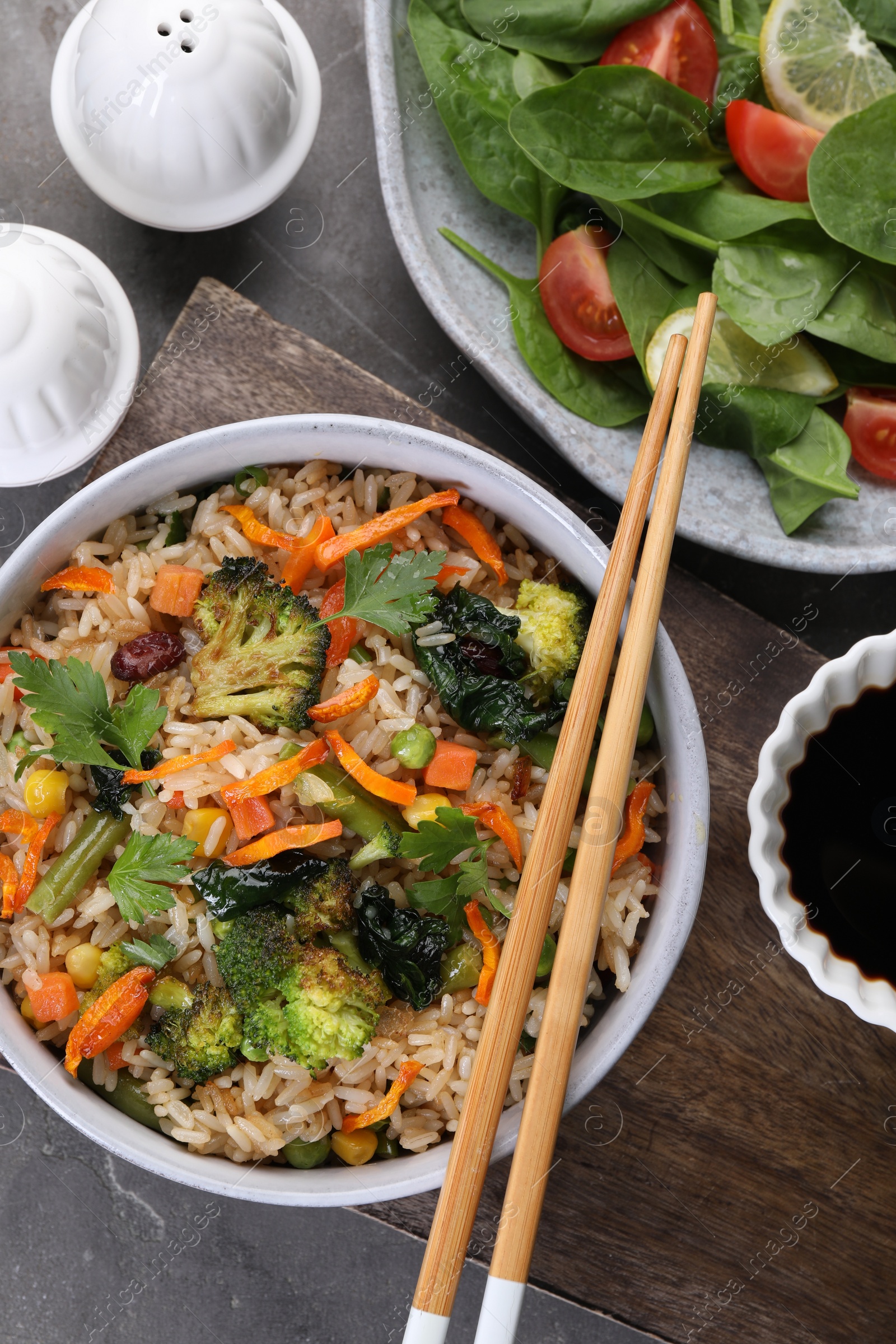 Photo of Tasty fried rice with vegetables served on grey table, flat lay