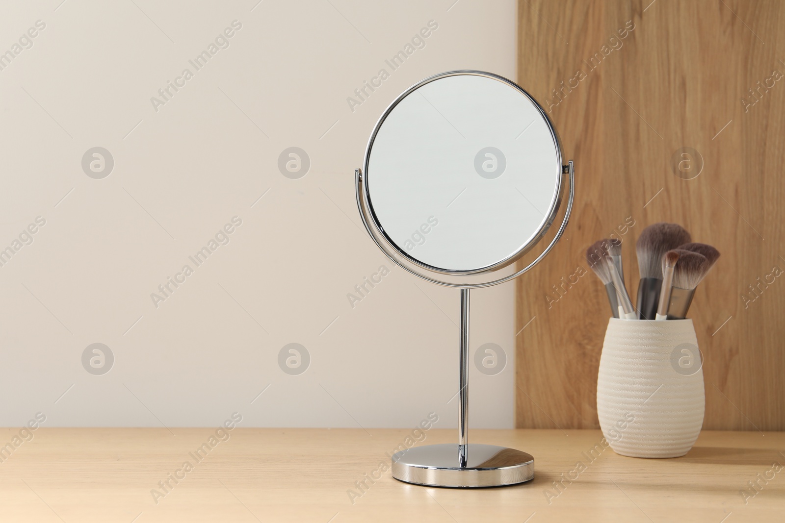 Photo of Mirror and makeup brushes on wooden dressing table in room. Space for text