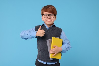 Photo of Smiling schoolboy with books showing thumb up on light blue background