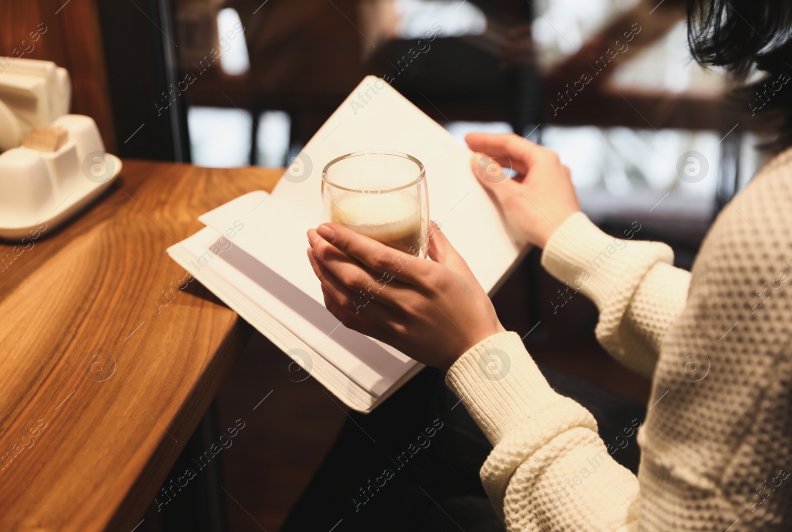 Photo of Woman with coffee reading book at wooden table, closeup