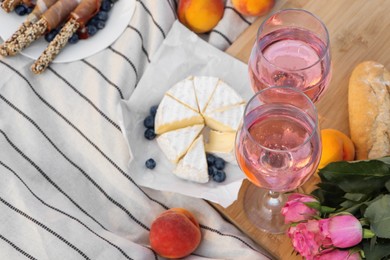 Photo of Glasses of delicious rose wine, flowers and food on white picnic blanket