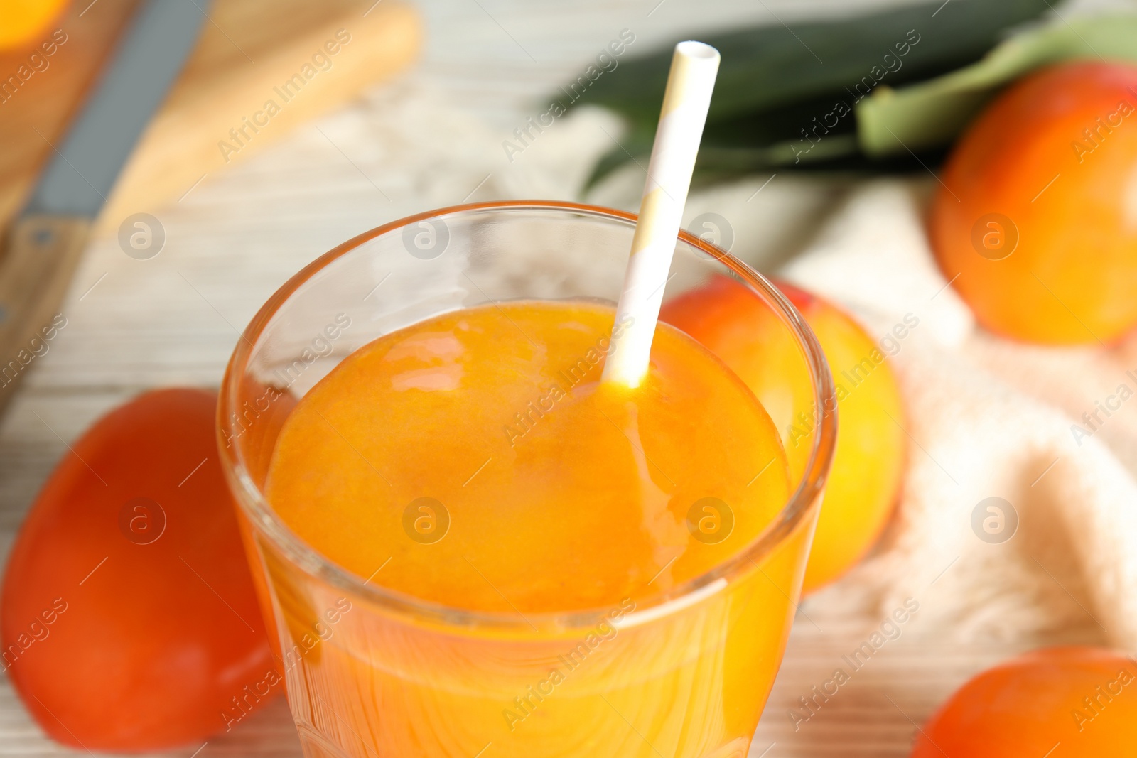 Photo of Tasty persimmon smoothie with straw on table, closeup