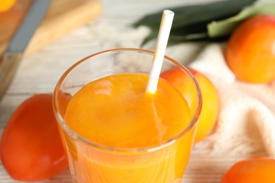 Tasty persimmon smoothie with straw on table, closeup