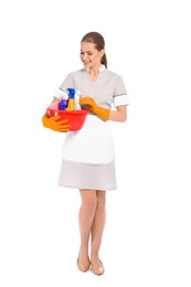 Young chambermaid holding basin with cleaning supplies on white background