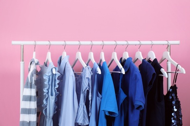 Rack with bright clothes on color background