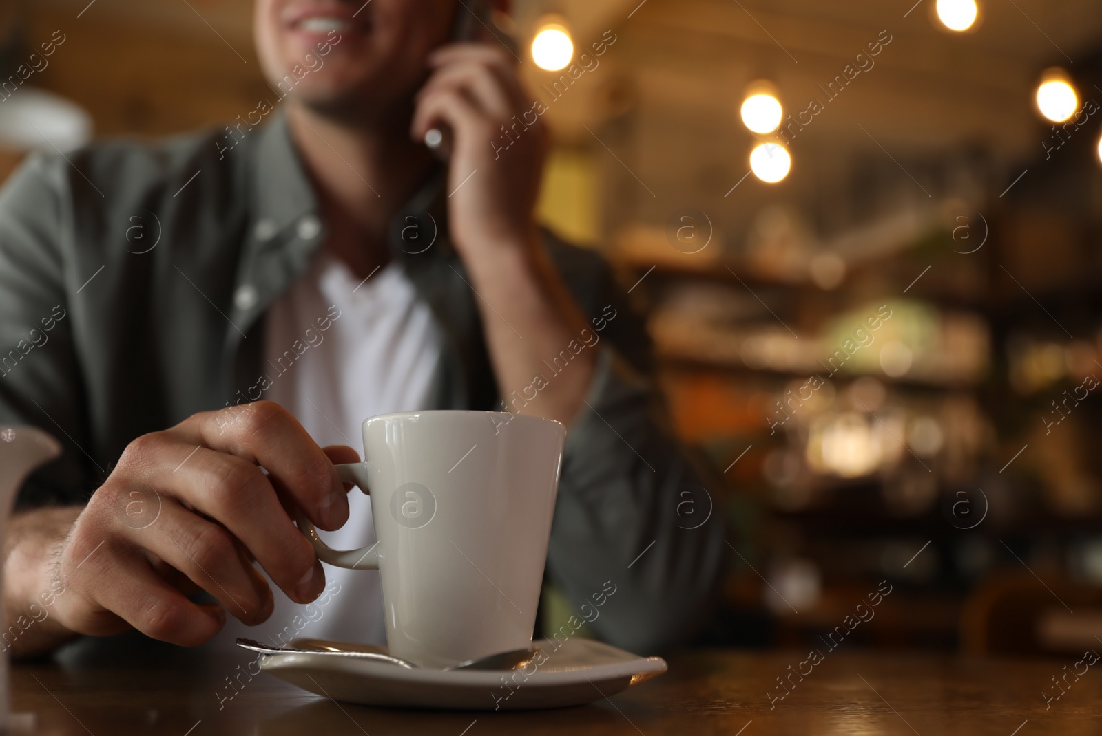 Photo of Man with cup of coffee talking on smartphone at cafe in morning, closeup. Space for text