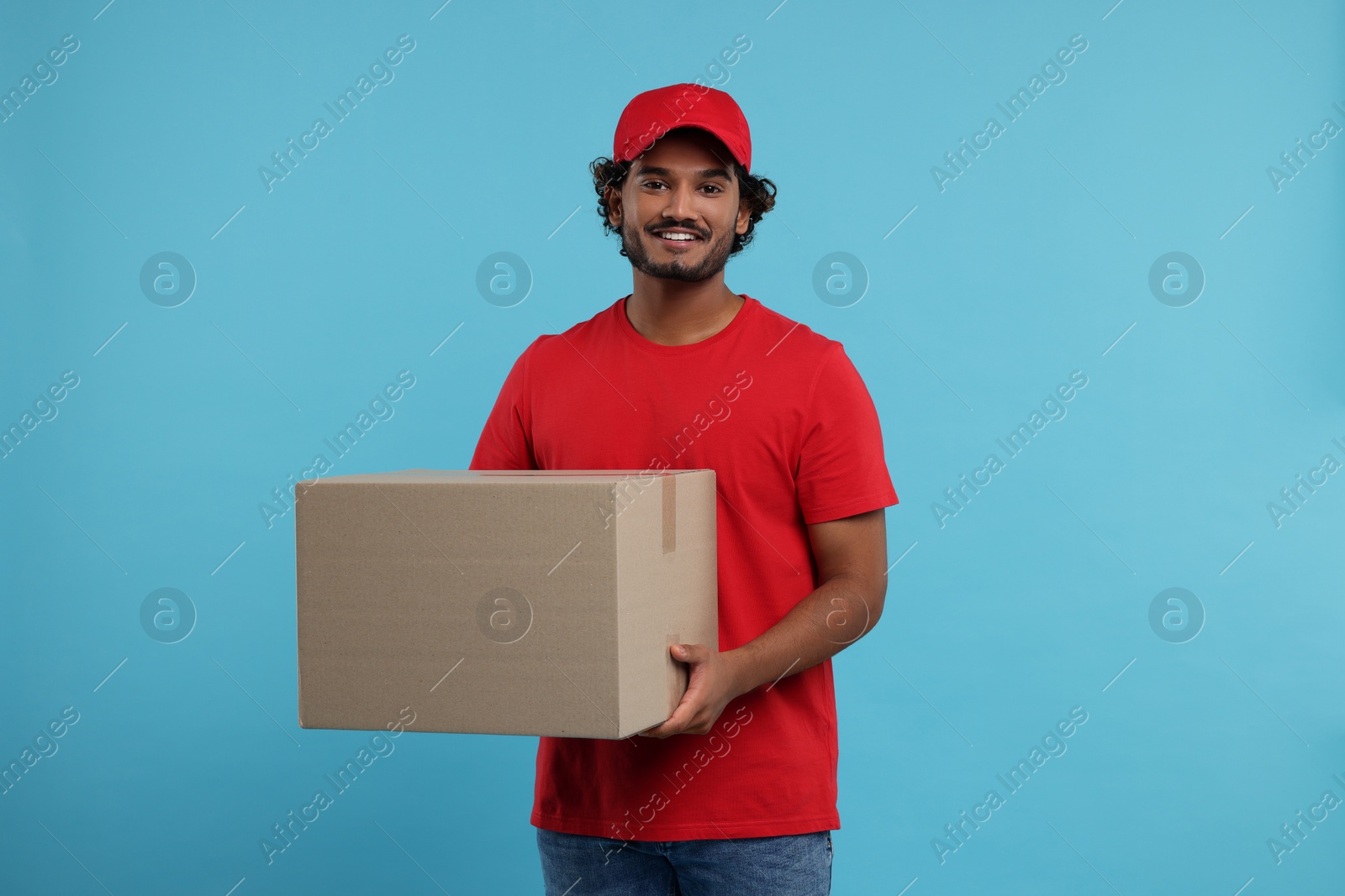 Photo of Happy young courier with parcel on light blue background