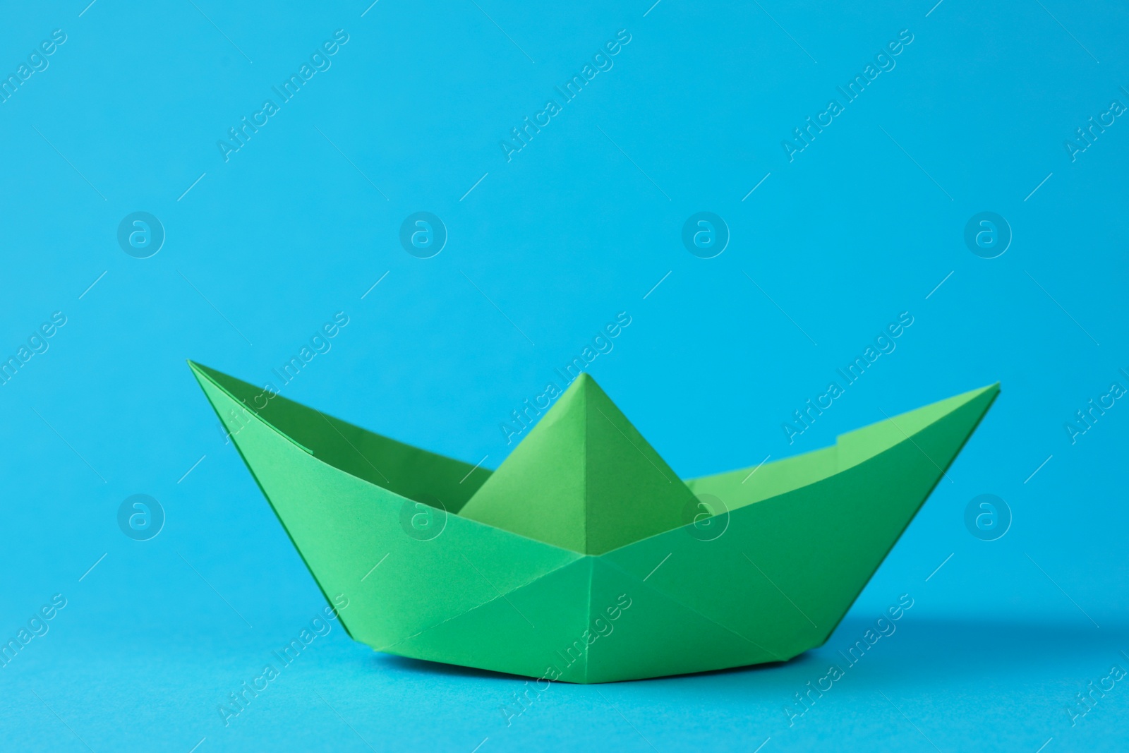 Photo of Handmade green paper boat on light blue background. Origami art