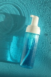 Bottle of cosmetic product in water on turquoise background, top view