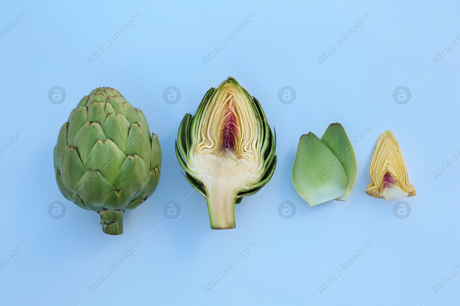 Photo of Whole and cut fresh raw artichokes on white background, flat lay