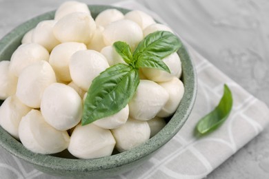 Photo of Tasty mozzarella balls and basil leaves in bowl on grey table, closeup. Space for text