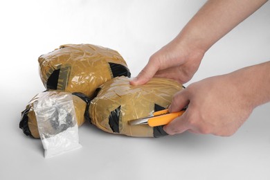 Photo of Smuggling and drug trafficking. Man opening package of narcotics with box cutter on white background, closeup