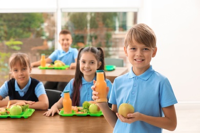 Photo of Happy boy holding bottle of juice and apple in school canteen. Healthy food