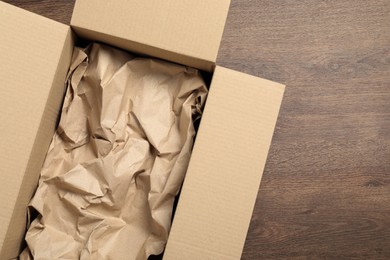 Photo of Open cardboard box with crumpled paper on wooden floor, top view and space for text. Packaging goods