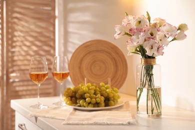 Photo of Bouquet of beautiful eustoma flowers, wine and grapes on white table indoors. Interior design