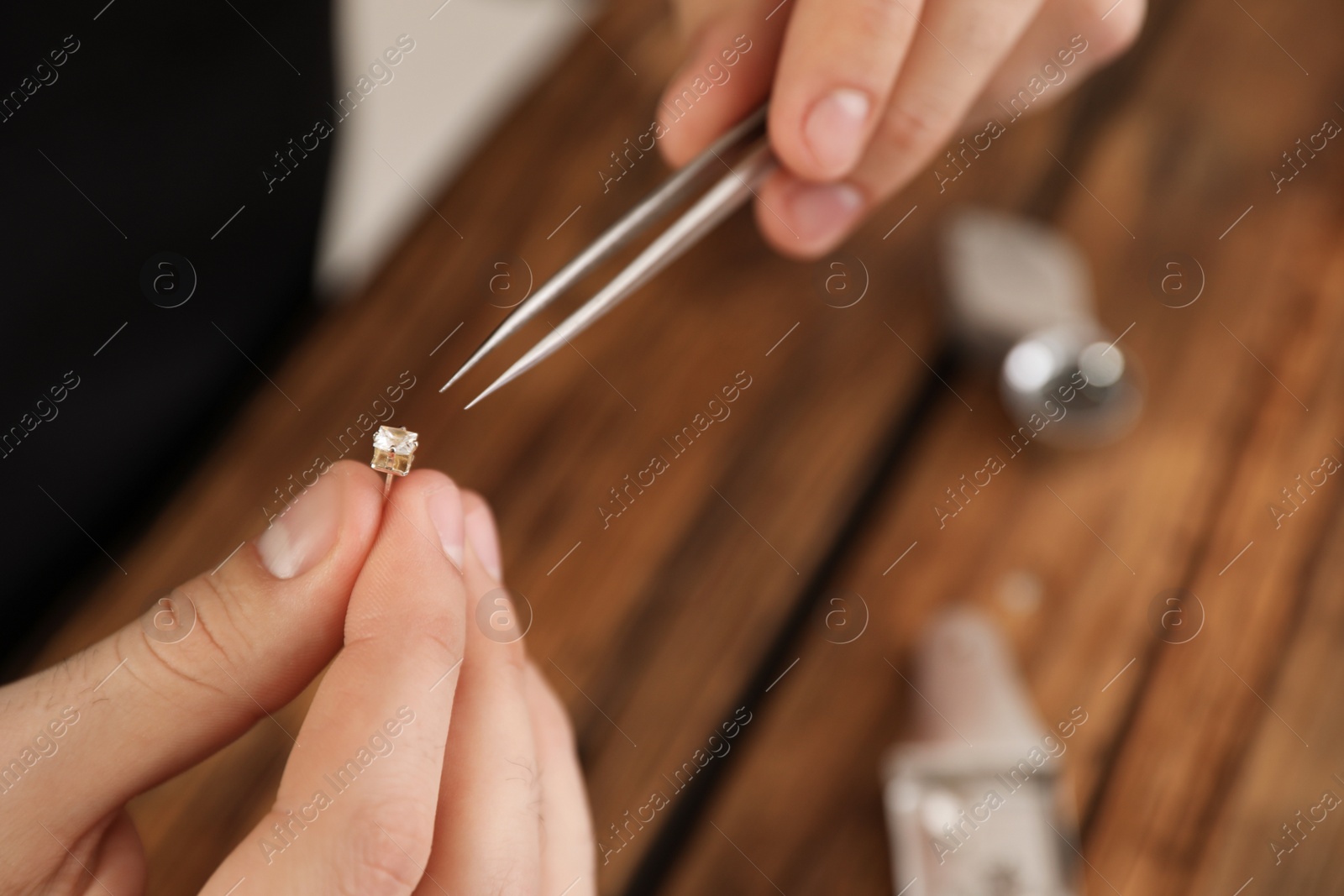 Photo of Male jeweler evaluating earring at table in workshop, closeup