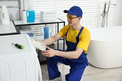 Photo of Smiling plumber wearing protective glasses repairing washing machine in bathroom