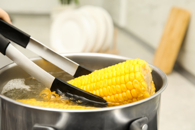 Photo of Taking boiled corn from pot with tongs in kitchen