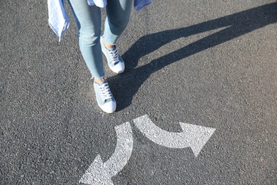 Image of Choice of way. Woman walking towards drawn marks on road, closeup. White arrows pointing in opposite directions