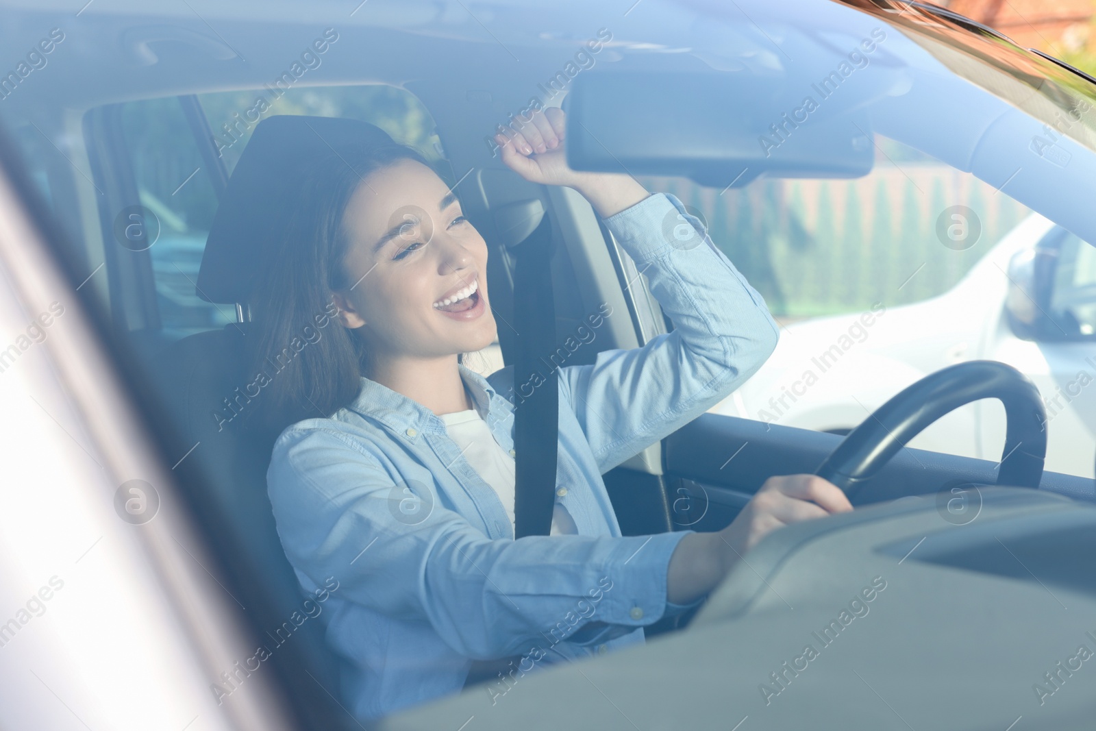 Photo of Listening to radio while driving. Emotional young woman enjoying music in car, view through windshield