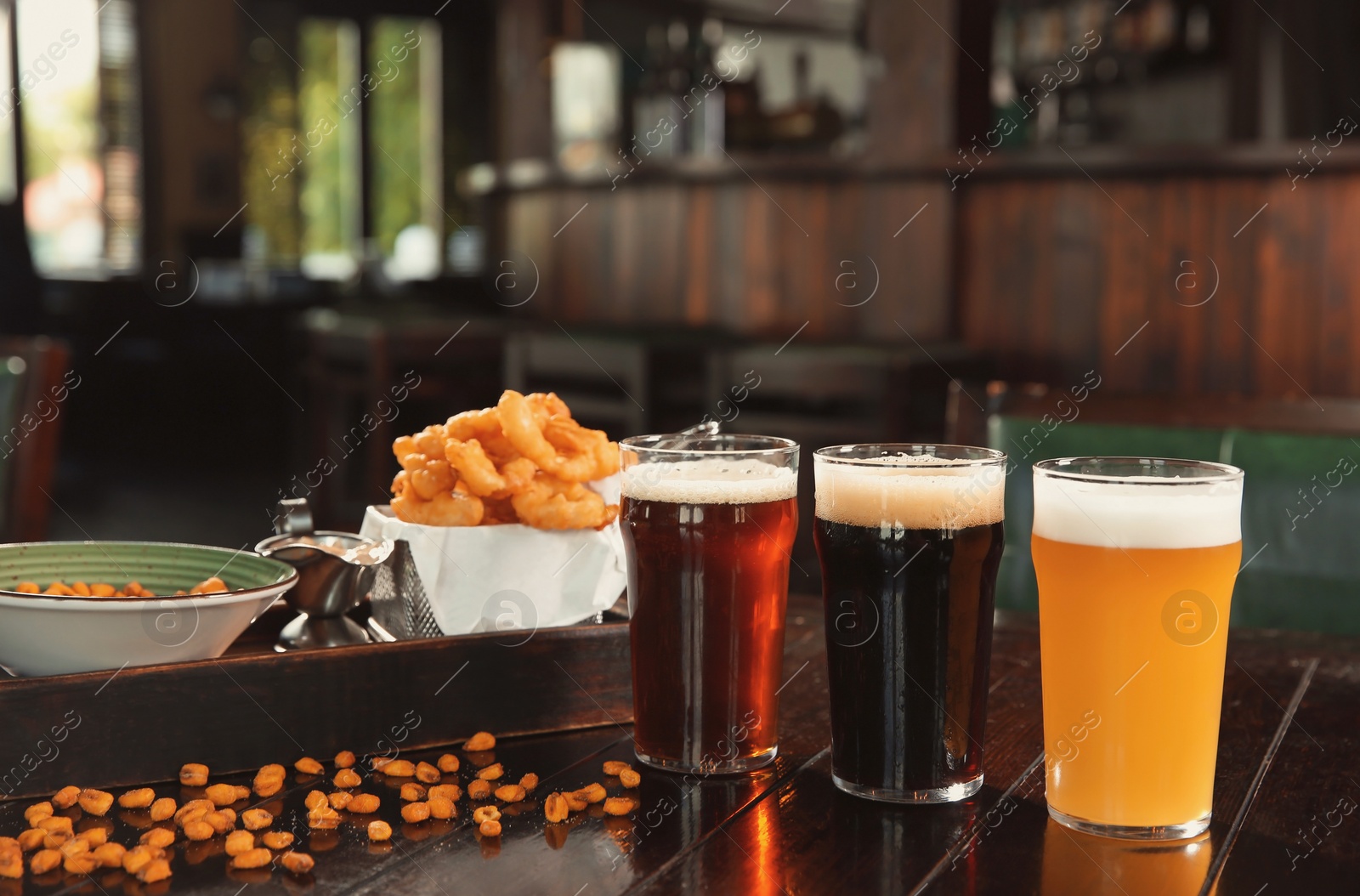 Photo of Glasses of tasty beer and snacks on wooden table in bar