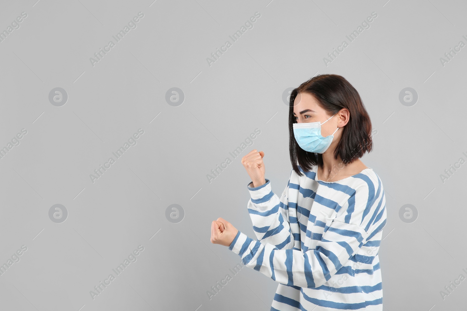 Photo of Woman with protective mask in fighting pose on light grey background, space for text. Strong immunity concept