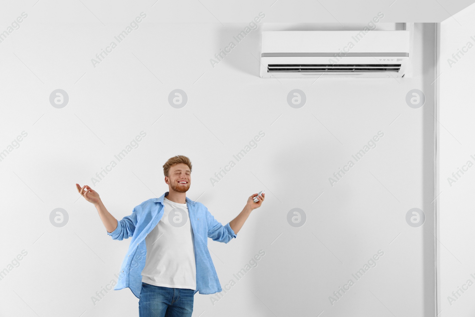 Photo of Young man operating air conditioner with remote control indoors. Space for text