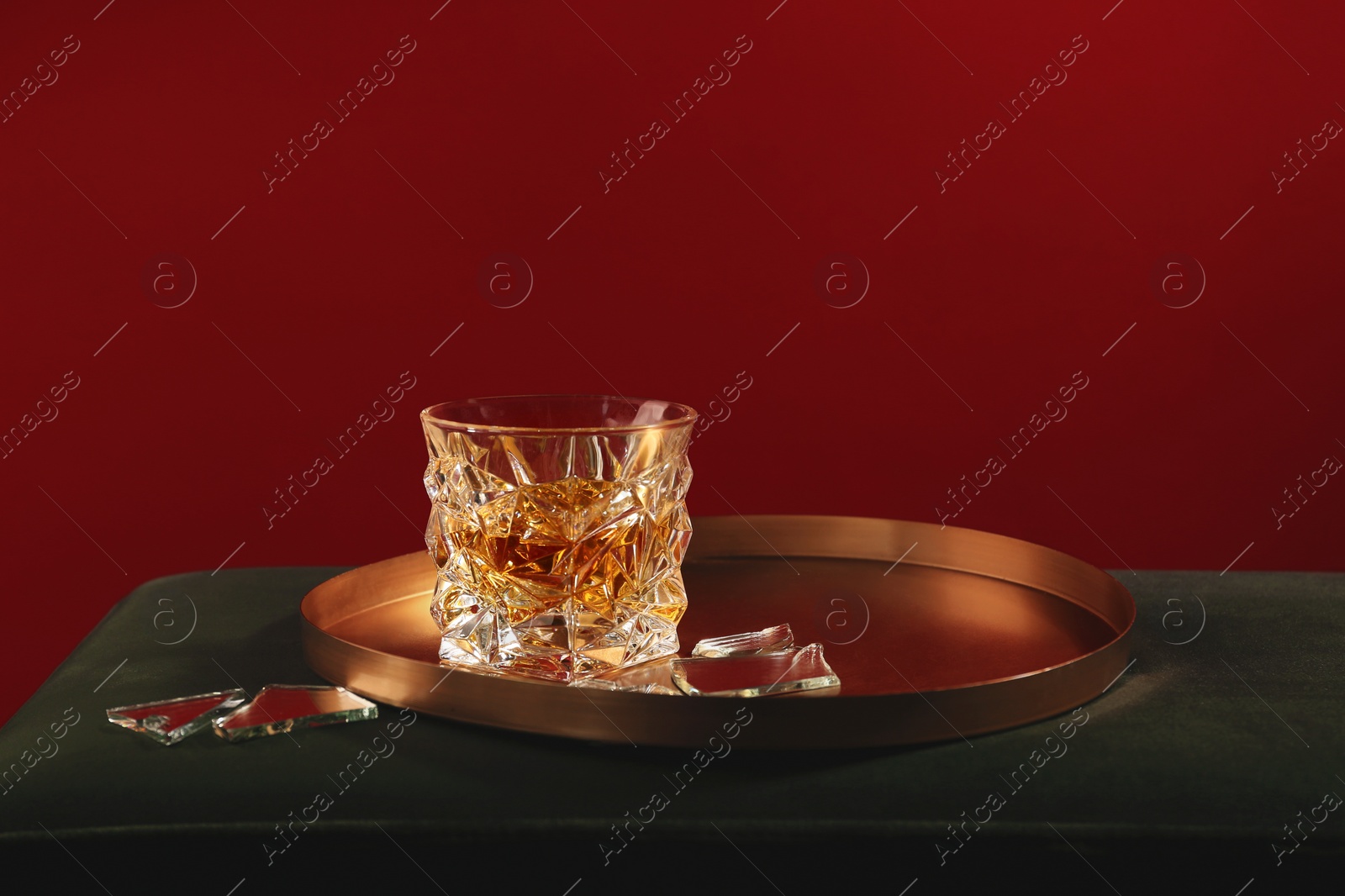 Photo of Glass of alcohol drink and shards of broken mirror on soft surface