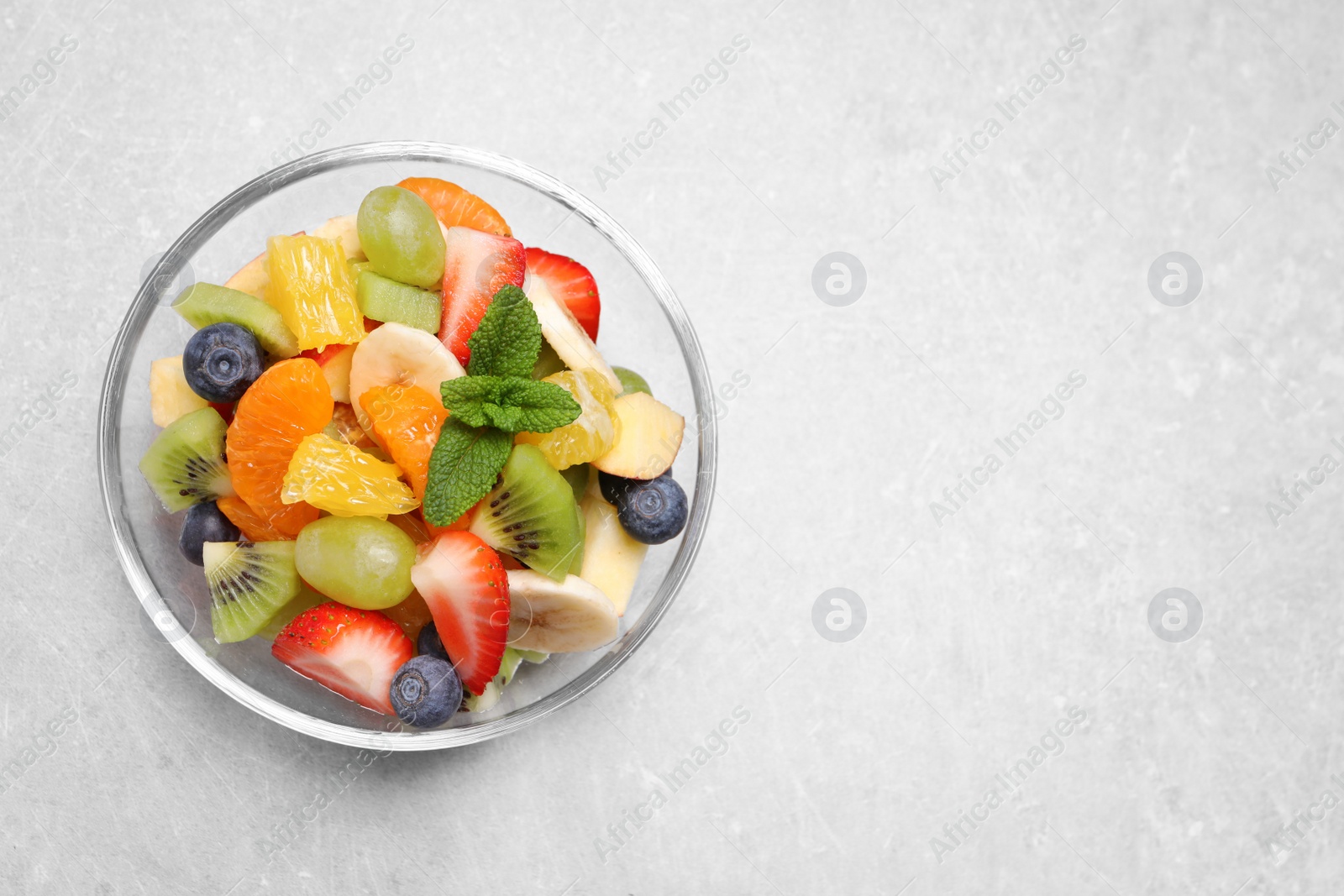 Photo of Delicious fresh fruit salad in bowl on light table, top view. Space for text