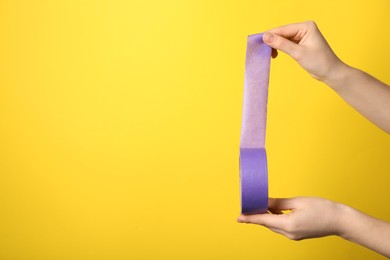 Photo of Woman holding violet adhesive tape on yellow background, closeup. Space for text