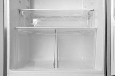 Photo of Modern open refrigerator with empty shelves, closeup