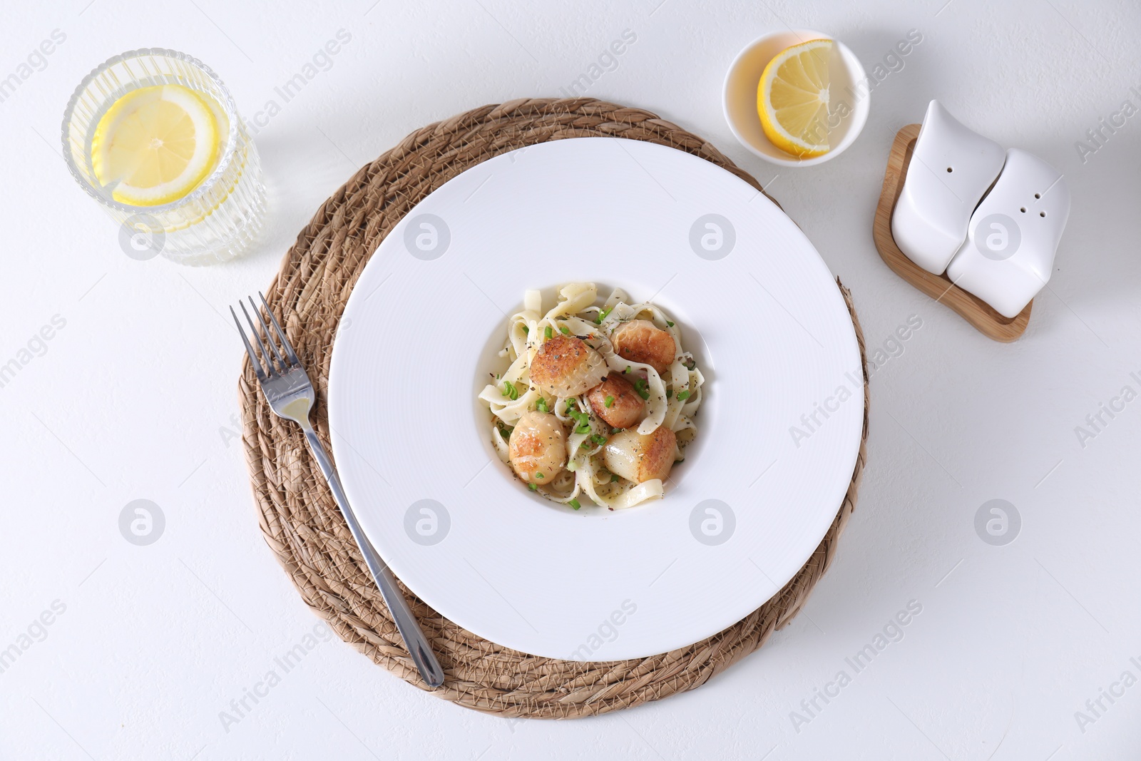 Photo of Delicious scallop pasta with spices in bowl served on white table, flat lay