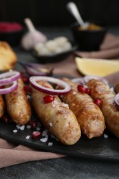 Photo of Tasty grilled sausages with onion rings and pomegranate seeds served on grey table, closeup