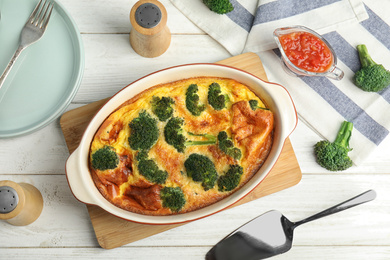 Tasty broccoli casserole in baking dish on white wooden table, flat lay