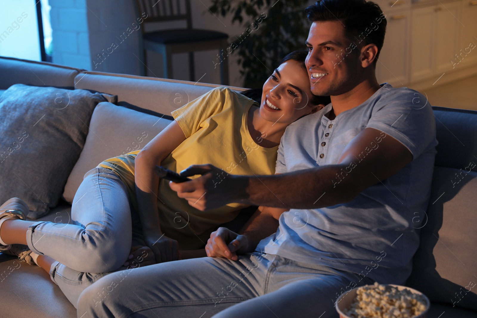 Photo of Couple watching movie with popcorn on sofa at night