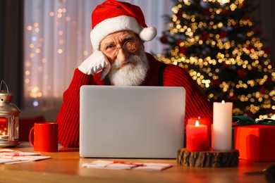 Santa Claus using laptop at his workplace in room with Christmas tree