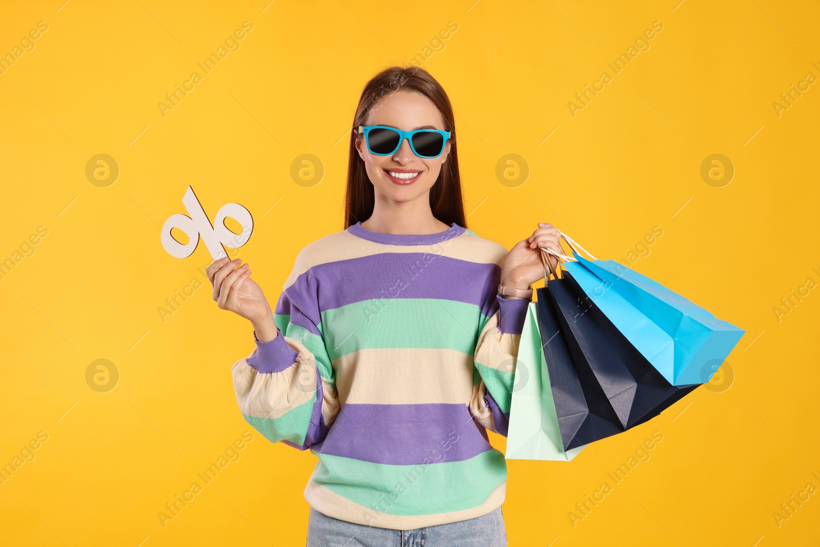 Photo of Happy young woman with shopping bags and percent symbol on yellow background. Big sale