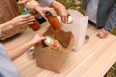 Photo of Group of volunteers packing food products at table outdoors, closeup