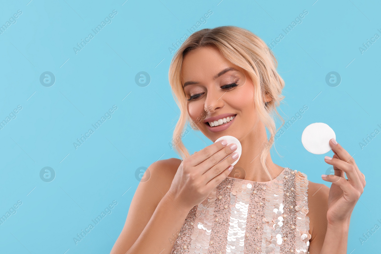 Photo of Smiling woman removing makeup with cotton pads on light blue background. Space for text