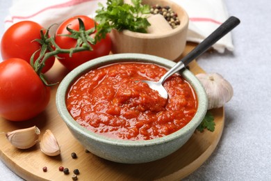 Photo of Homemade tomato sauce in bowl, spoon and fresh ingredients on light grey table