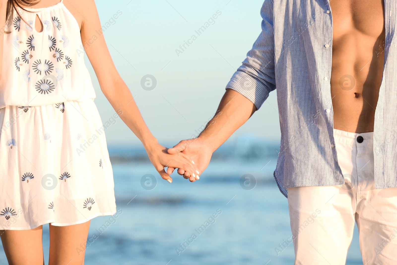 Photo of Happy young couple holding hands at beach on sunny day, closeup