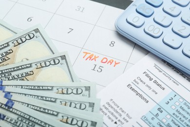 Photo of Tax day. Document, dollar banknotes and calculator on calendar with date reminder