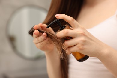 Woman applying oil hair mask indoors, closeup